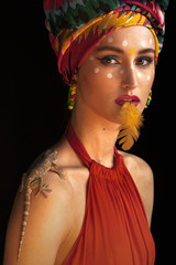 The model poses in the image of an Oriental Princess in a photo Studio on a dark background. model in a bright outfit a bird feather on his lips and with a lizard on his shoulder
