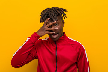 Young fitness african man blink at the camera through fingers, embarrassed covering face.
