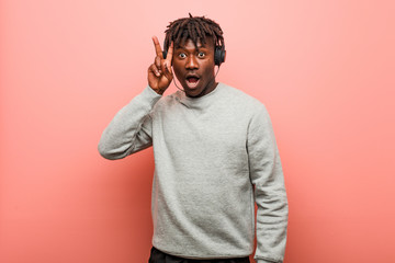 Young rasta black man listening to music with headphones showing victory sign and smiling broadly.