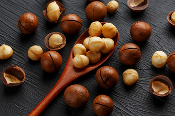 Shelled macadamia nut and peeled macadamia nut on a black textural background in a wooden spoon