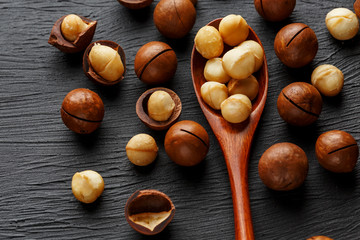Shelled macadamia nut and peeled macadamia nut on a black textural background in a wooden spoon