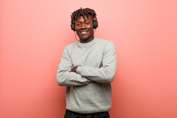 Young rasta black man listening to music with headphones smiling confident with crossed arms.