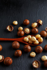 Obraz premium Shelled macadamia nut and peeled macadamia nut on a black textural background in a wooden spoon