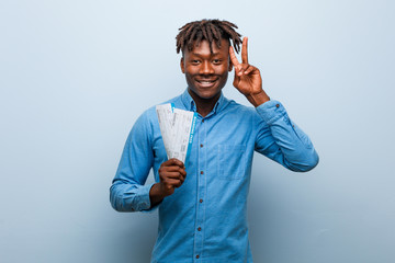 Young rasta black man holding an air tickets showing victory sign and smiling broadly.
