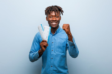 Young rasta black man holding an air tickets showing fist to camera, aggressive facial expression.