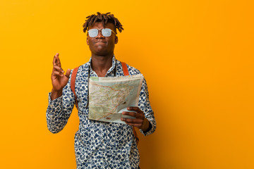 Young rasta black man holding a map crossing fingers for having luck