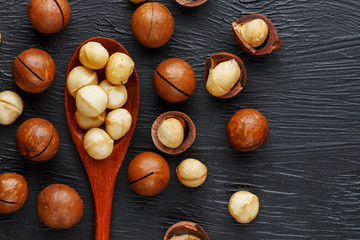 Shelled macadamia nut and peeled macadamia nut on a black textural background in a wooden spoon