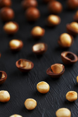 Purified and shell repeats macadamia nuts on black textural stone background. Healthy eating concept