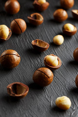 Obraz premium Purified and shell repeats macadamia nuts on black textural stone background. Healthy eating concept