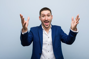 Young business caucasian man receiving a pleasant surprise, excited and raising hands.