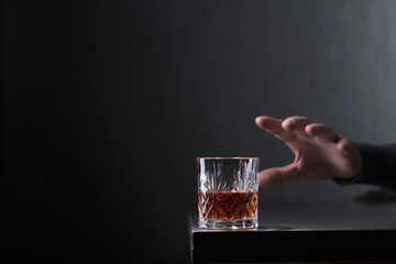Man's hand reaches for a glass of alcohol.