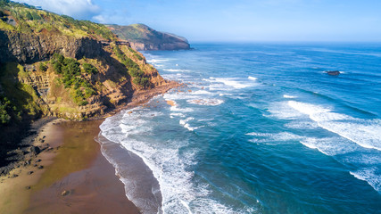 Surf on the beach on sunny day with rocky cliffs on the background. Auckland, New Zealand