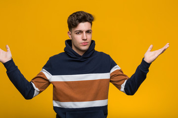 Fototapeta premium Young cool man wearing a hoodie doubting and shrugging him shoulders in questioning gesture.