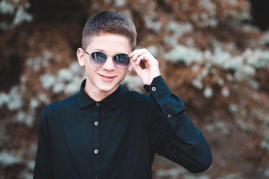 Smiling teen boy 15-16 year old wearing sun glasses outdoors over nature  background. Looking at camera. Teenagerhood. Stock Photo