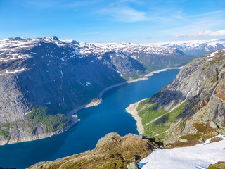 Naklejka na ściany i meble A panoramic view from above on a fjord-like Ringedalsvatnet lake, Norway . Snow-capped mountains. Spring slowly coming to the higher parts of the mountains. Water of the lake has a navy blue shade.