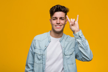 Young handsome student wearing a denim shirt showing a horns gesture as a revolution concept.