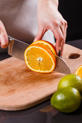 young woman in a gray aprons cuts an orange