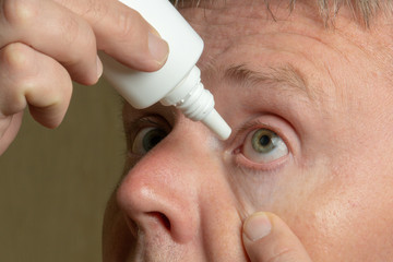 Close-up portrait of a white man using eye drops from a small white bottle