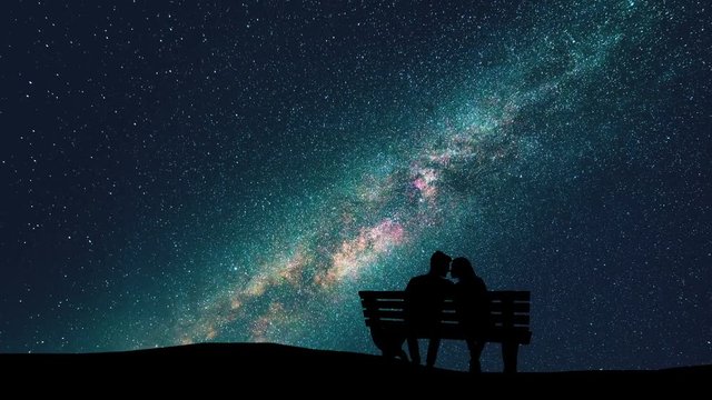 The man and woman sitting on a bench on the starry sky background. time lapse