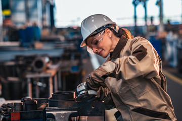Female heavy industry worker in protective work wear grinding metal. - obrazy, fototapety, plakaty