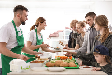 Obraz na płótnie Canvas Volunteers giving food to poor people indoors