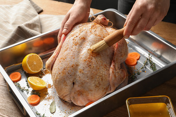 Woman marinating whole turkey at table, closeup