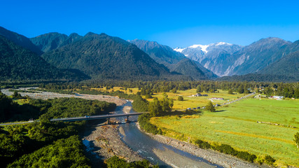 Bridge across the river in the middle of sunny valley with snowy mountains on the background. West Coast, South Island, New Zealand