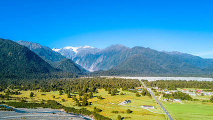Road running through sunny valley with high mountains on the background. West Coast, South Island, New Zealand
