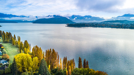 Small town surrounded by yellow autumn trees on a shore of pristine lake with mountains on the...