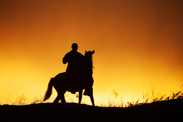 Silhouette of rider on horseback and beautiful orange sunset