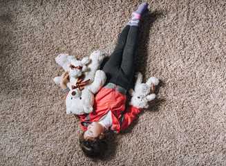 A little caucasian funny child girl fell asleep with three teddy bears while playing on the carpet. Midday sleep. Top view, upside down.