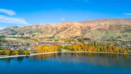Small town surrounded by yellow autumn trees on a shore of pristine lake with mountains on the background. Wanaka, Otago, South Island, New Zealand