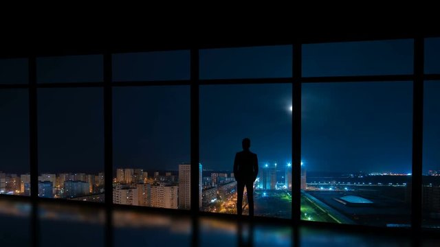 The man standing near the window on the night city background. time lapse