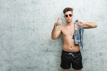 Young caucasian man wearing a swimsuit showing thumbs up and thumbs down, difficult choose concept