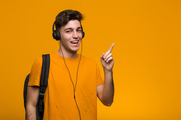 Young cool student man listening to music with headphones pointing with finger at you as if inviting come closer.