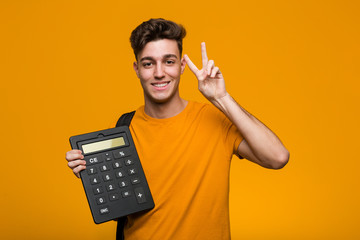 Young student man holding a calculator looking sideways with doubtful and skeptical expression. - obrazy, fototapety, plakaty