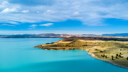 Hills on a shore of a beautiful lake with mountain range on the background. Otago, South Island, New Zealand