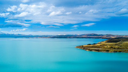 Hills on a shore of a beautiful lake with mountain range on the background. Otago, South Island, New Zealand