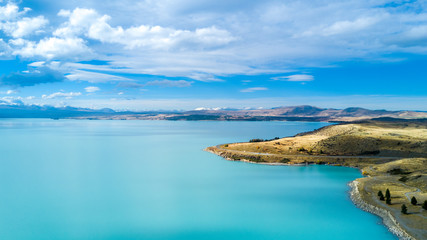 Hills on a shore of a beautiful lake with mountain range on the background. Otago, South Island, New Zealand
