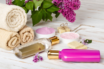 Obraz na płótnie Canvas Spa and bath cosmetics with lilac flowers. Hair care (shampoo, shower gel, balm, mask, bath salt, soap and towel rolls on wooden rustic background. Organic natural cosmetics for hairs and body, spring