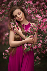 Romantic portrait of young attractive woman in blooming pink apple garden
