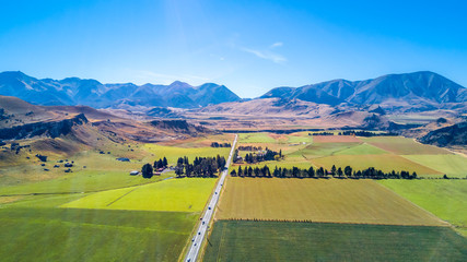 Road running through farmland with mountains on the background. West Coast, South Island, New...