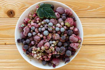 frozen berries, black currant, red currant, raspberry, blueberry in bowl decorated by currant leaf on wooden table in rustic style,  top view. - 267634275