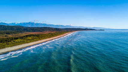 Sunset over remote beach on the coast on Tasman sea with native forest and mountains on the background. West Coast, South Island, New Zealand