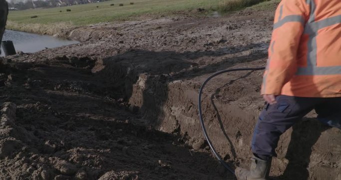 man laying hose in trench whille excavator is making trenche