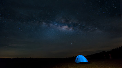 Fototapeta na wymiar Camping under the stars. The Milky Way stretches overhead a blue tent high In the pasture .