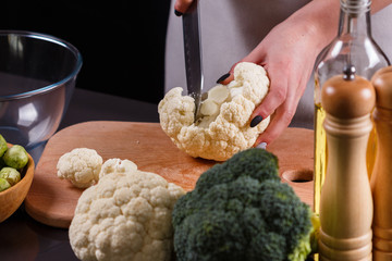young woman in a gray aprons cuts cauliflower broccoli