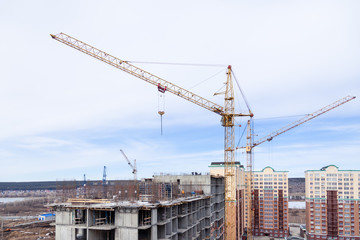 High-rise mighty hoisting crane and large building construction site with cranes with long yellow arrow against blue sky new multi-storey concrete brick, industrial background