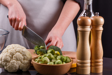 young woman in a gray aprons cuts cauliflower broccoli