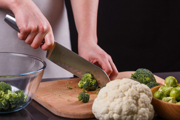young woman in a gray aprons cuts cauliflower broccoli